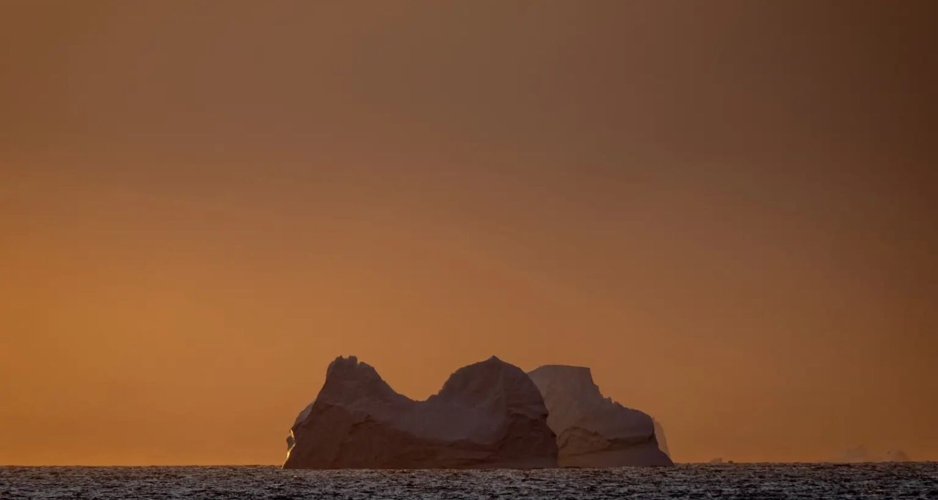 a view of a glacier in the ocean with an orange sky behind it