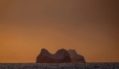 a view of a glacier in the ocean with an orange sky behind it