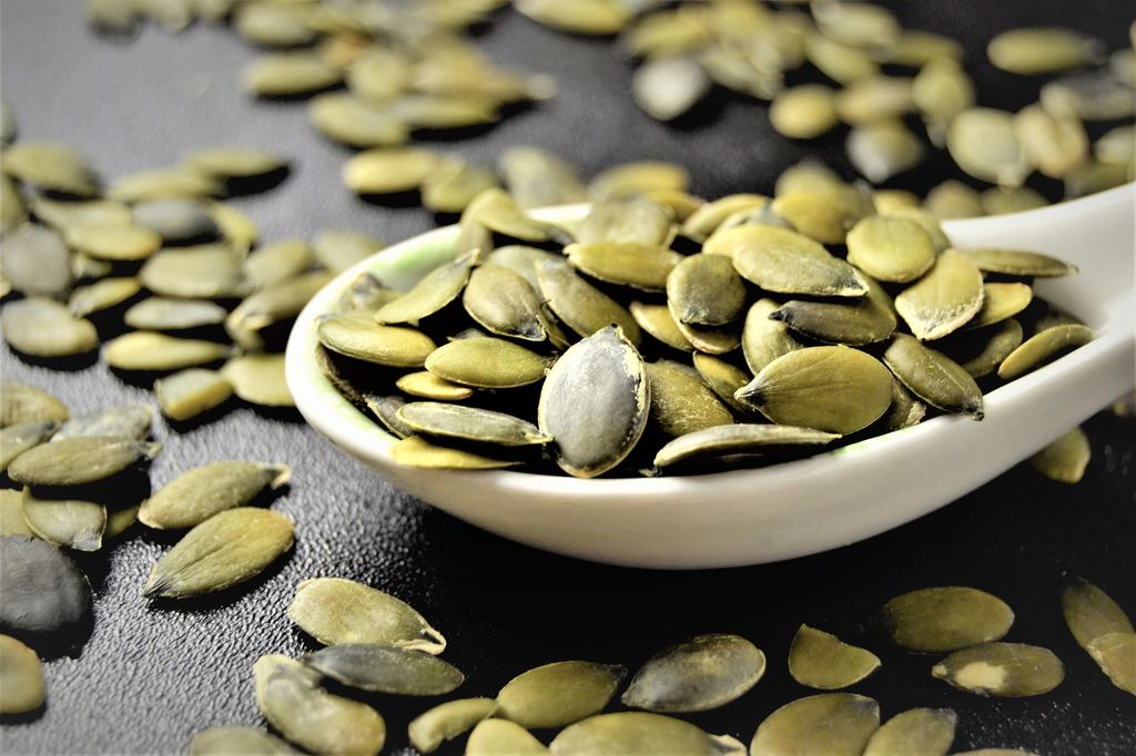 Pumpkin seeds on a spoon in black background, close-up