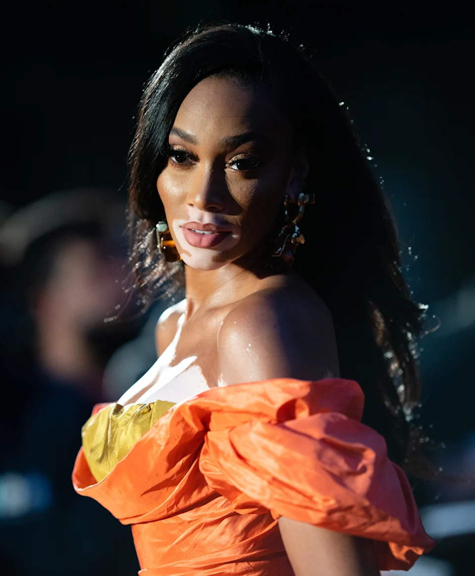 Winnie Harlow poses on a red carpet wearing an off-the-shoulder gown with voluminous sleeves
