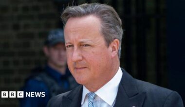 Lord Cameron looking off site. He's wearing a dark suit and blue tie.