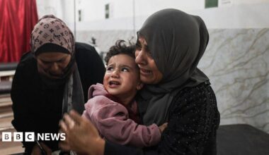 Crowds gather around a burnt out and destroyed car targeted by an Israeli airstrike in Gaza City.