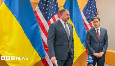 Andriy Yermak and Marco Rubio stand in front of Ukrainian and US flags in a conference room. Yermak is wearing a grey tie, and Rubio a red one.