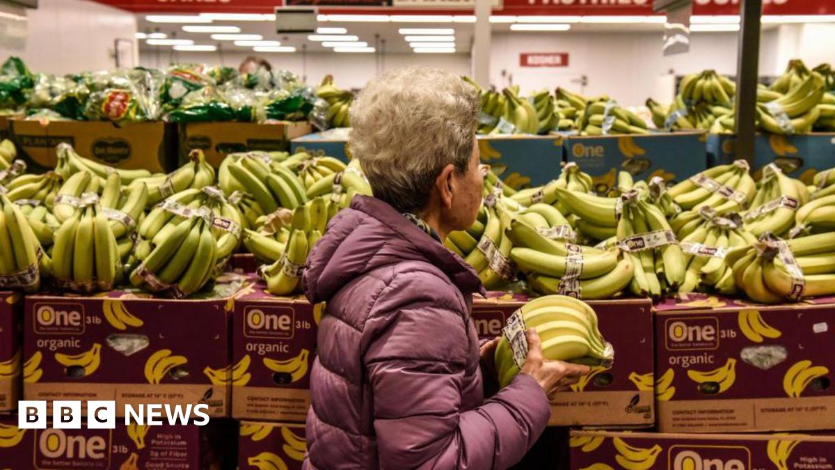 A woman holds bananas while walking through a grocery store aisle.