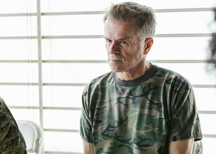 Middle-aged man in a camouflage shirt sitting thoughtfully in a bright room, reflecting on unforgettable psychiatric institution work experiences.
