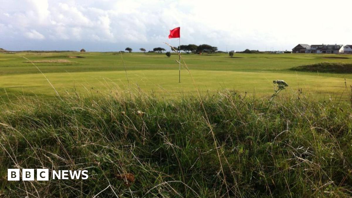 Golf course with red flag standing in hole and long grass bordering the fairway.