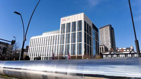 Sheffield Hallam University A large and tall modern building with several windows overlooks a long, steel wall outside Sheffield railway station