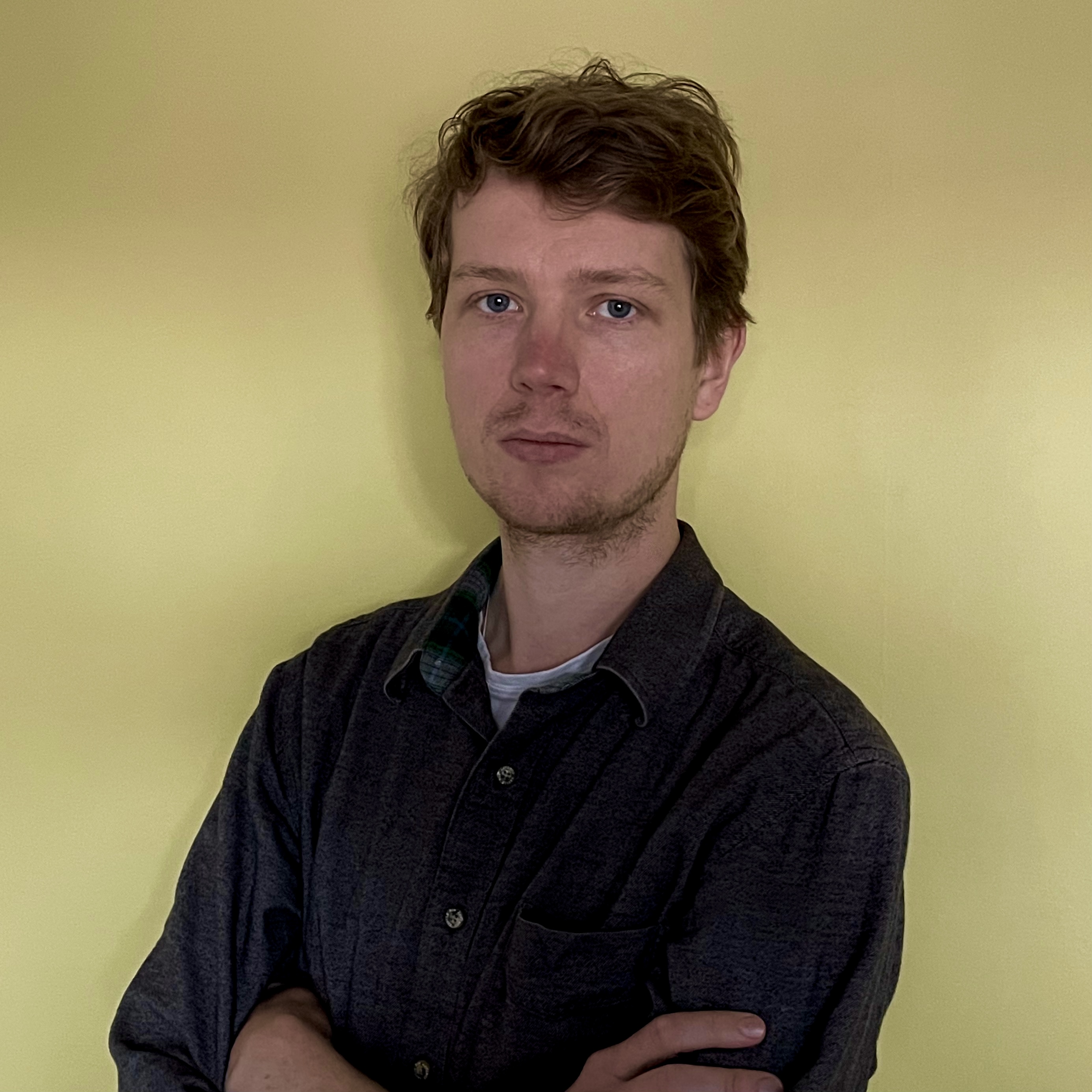 A man in a shirt looks at the camera, with a yellow background