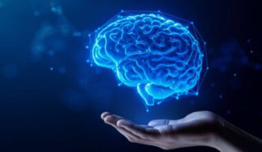 An outstretched hand underneath an artificial brain surrounded by blue digital neural points, representing the concept of AI.