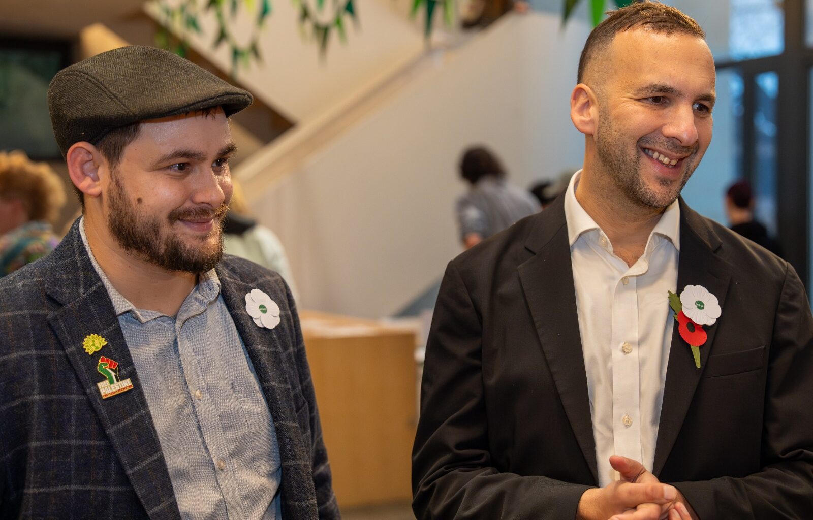 Two men in suits stand next to each other smiling.