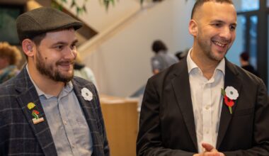 Two men in suits stand next to each other smiling.