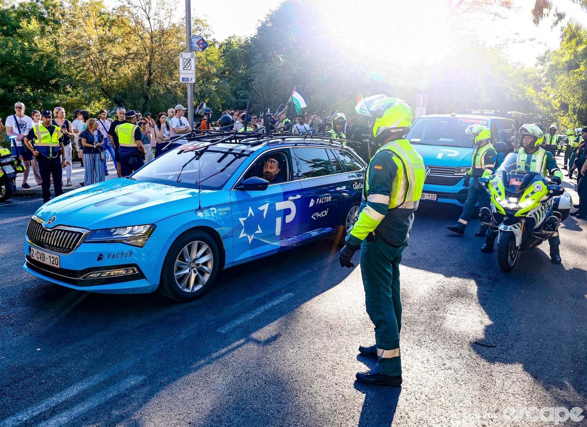 Israel-Premier Tech team vehicles drive past heavy security to the start of a 2025 Vuelta a España stage.