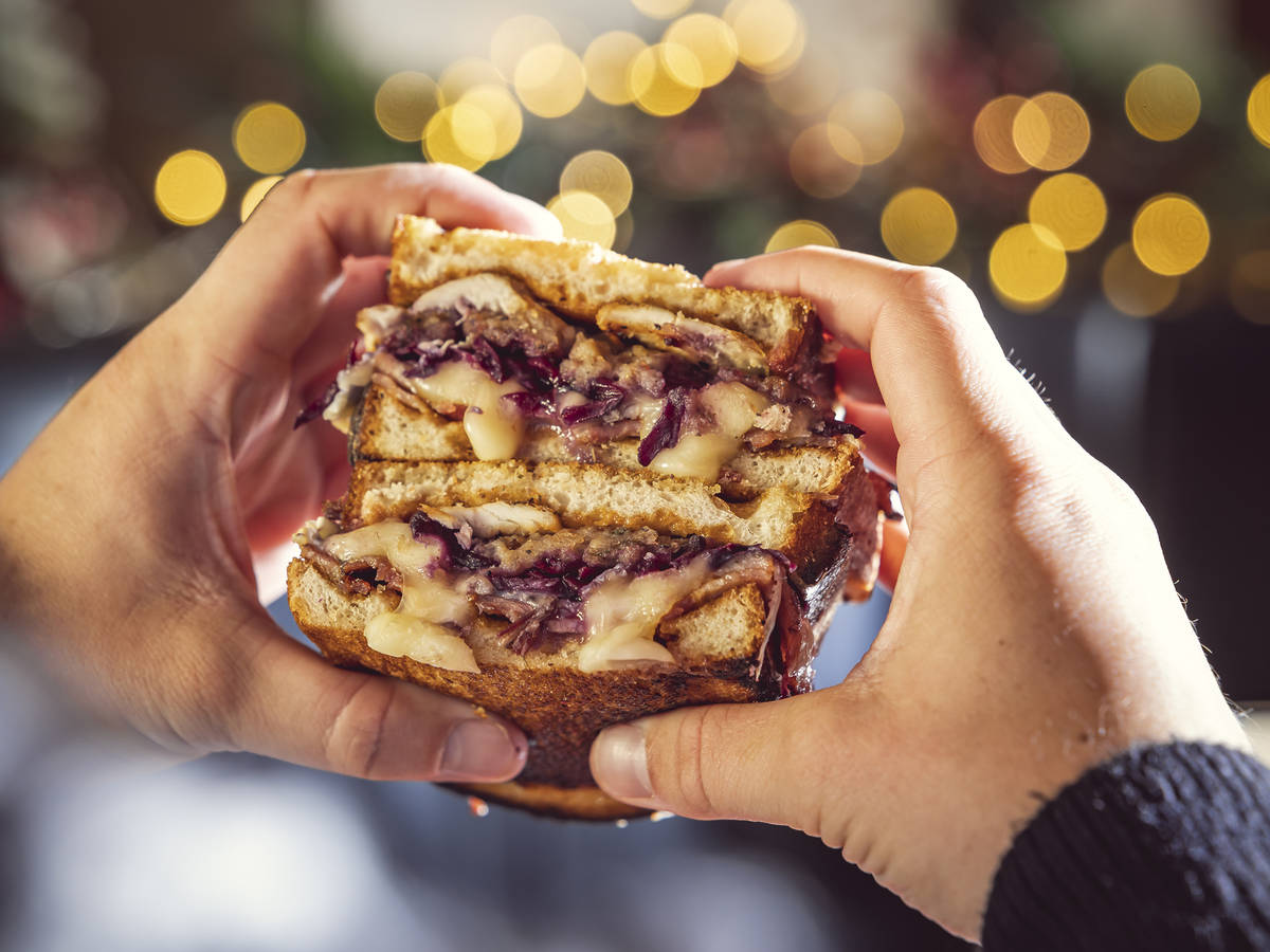 two halves of a christmas sandwich, dripping with sauce and filling, being held stacked on top of each other in two hands