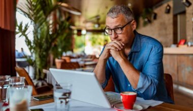 Middle-aged white man wearing glasses, staring into space over the top of his laptop in a coffee shop