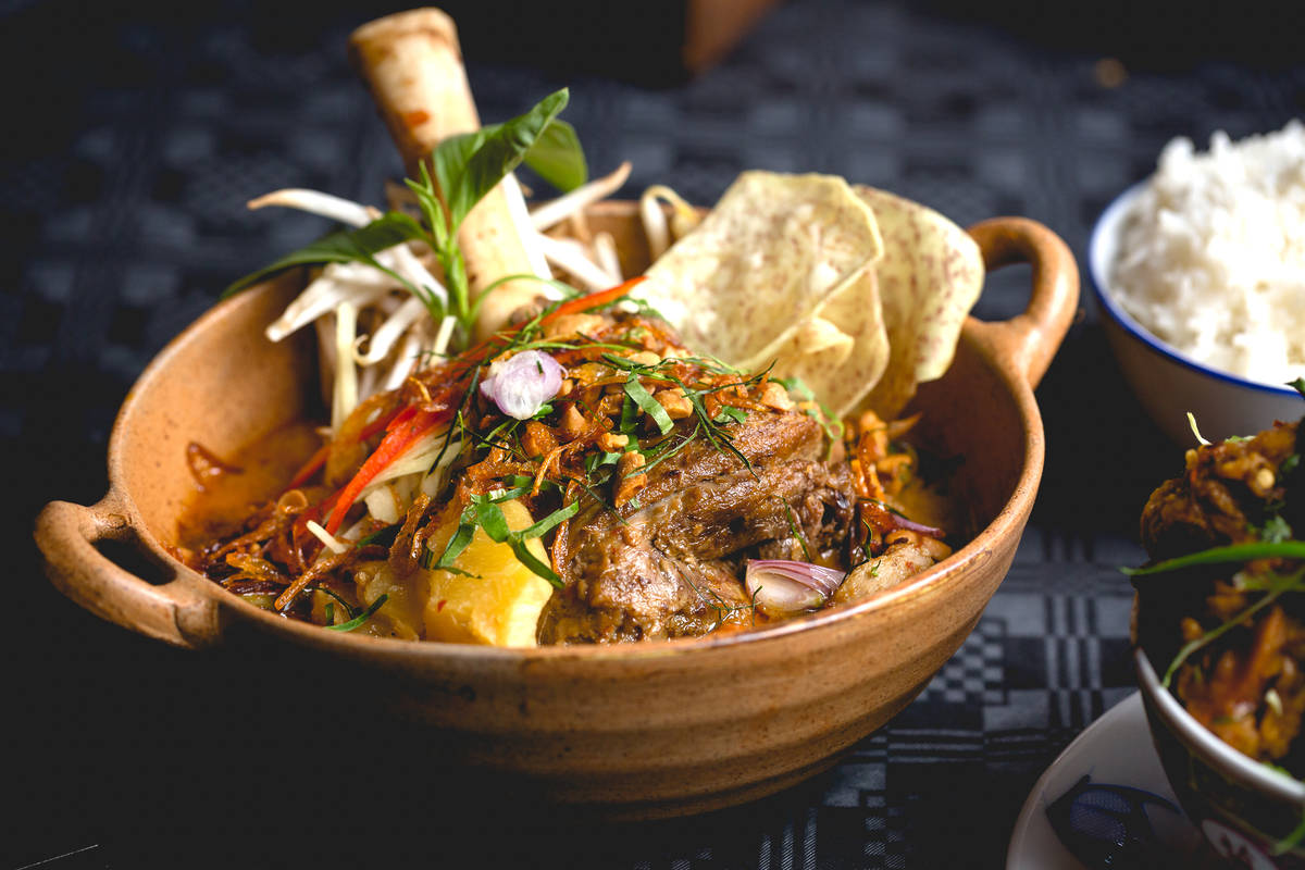 a ceramic bowl filled with a thai beef shin curry, a bone sticking out the back of the dish
