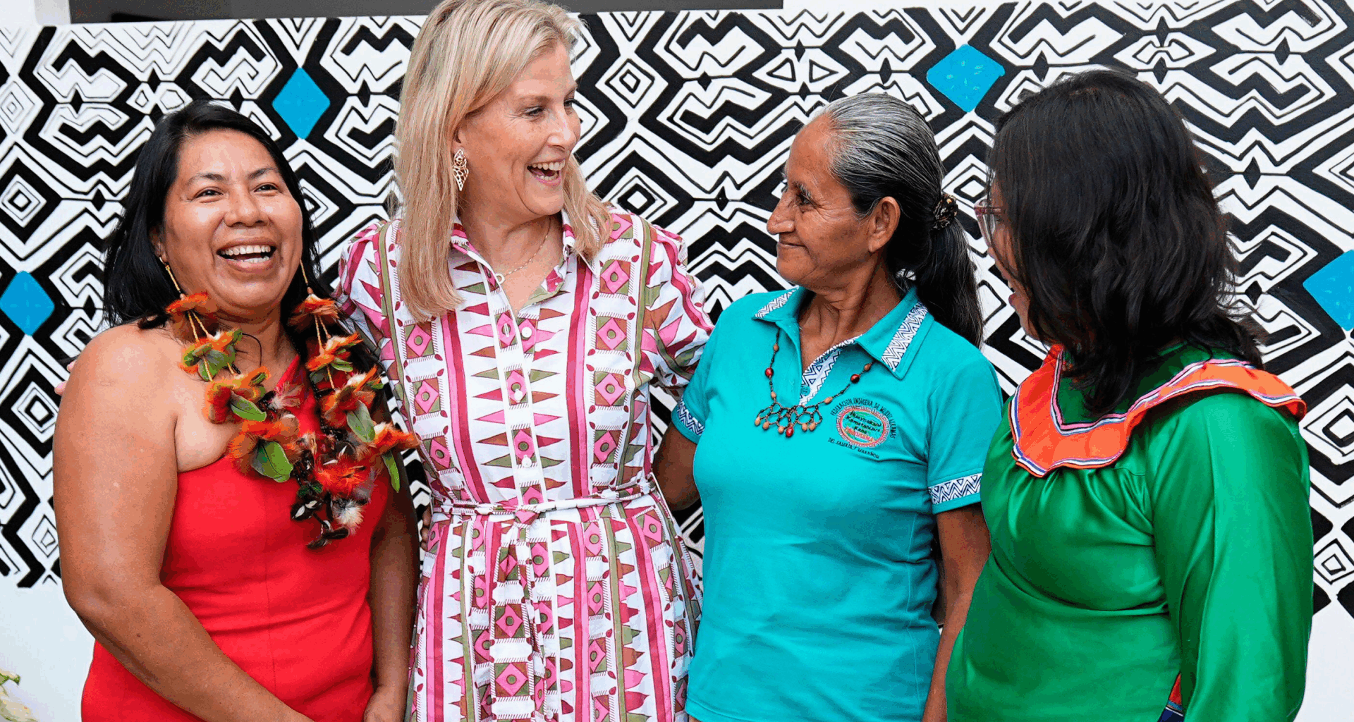 Duchess Sophie wearing a patterned shirt dress with her arms around three ladies and laughing