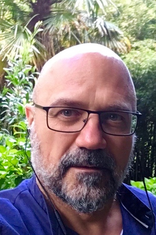 Bald man with eyeglasses and short salt-and-pepper beard, wearing a blue shirt.