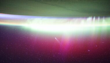 A streak of white showing Comet Lemmon moves into a red and green aurora seen on the edge of Earth in space