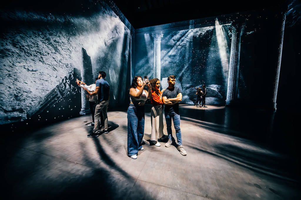 People gaze at walls depicting ash covered ruins at The Last Days of Pompeii: The Immersive Exhibition