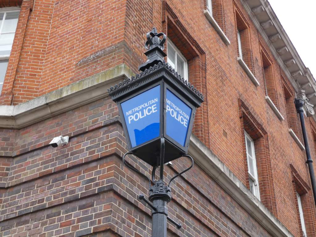 A lamp with 'Metropolitan Police' in white on blue glass outside a police station