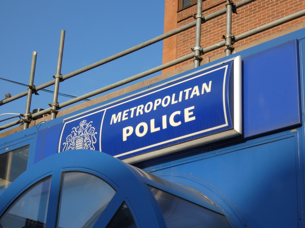 The 'Metropolitan Police' logo in white on a blue background on the side of a portakabin