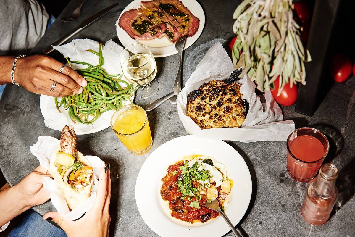 a table laid with food from Miznon and hands reaching in to grab things