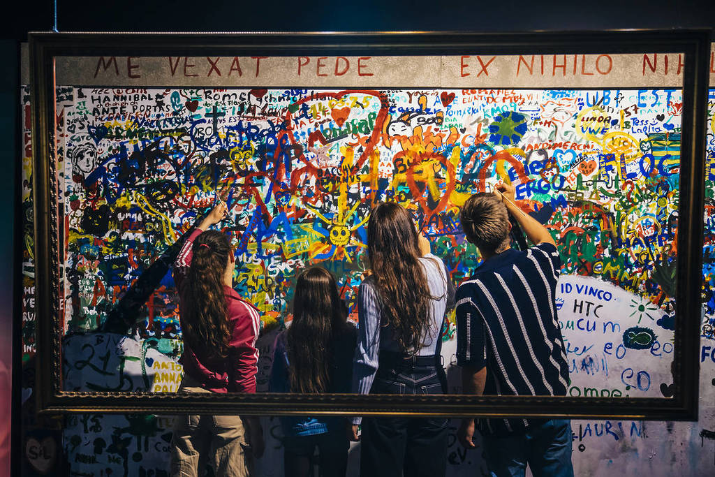 four people draw on a graffiti wall at The Last Days of Pompeii: The Immersive Exhibition
