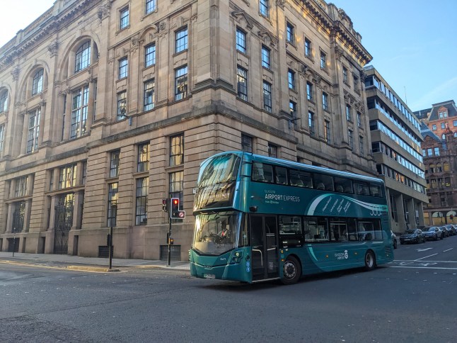Glasgow, UK - July 13 2025: The modern Glasgow Airport Express 500 bus service travels through the city centre, passing grand historical sandstone architecture on a clear day