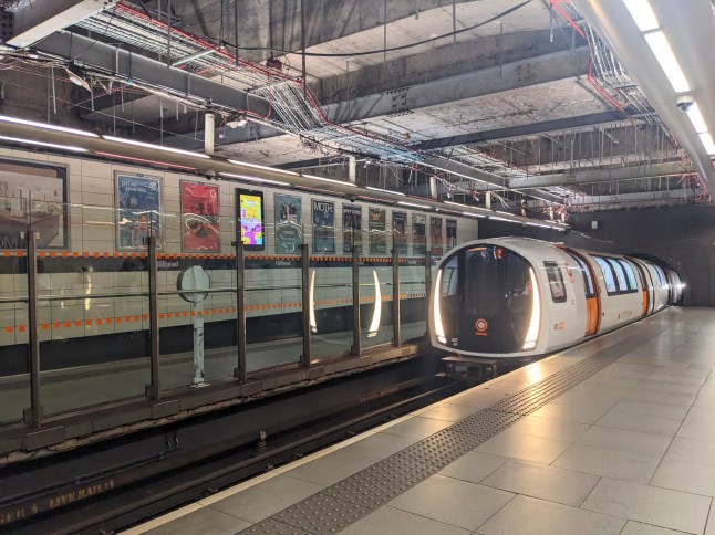 Glasgow, Scotland - July 13 2025: A modern white and orange train on the historic Glasgow Subway system arrives at the illuminated, industrial-style Hillhead station platform