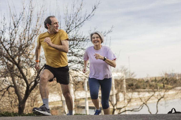 Cheerful senior couple jogging in a park, enjoying their active lifestyle and each other's company while surrounded by beautiful scenery