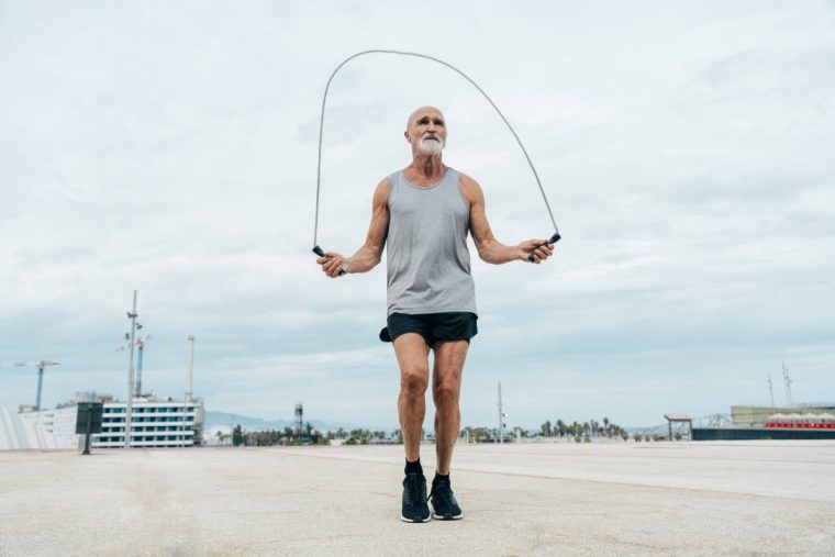 Fit retired senior man exercising with jump rope on footpath