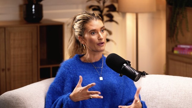Charley Webb wears a blue jumper during a podcast recording, sitting in front of a mic.