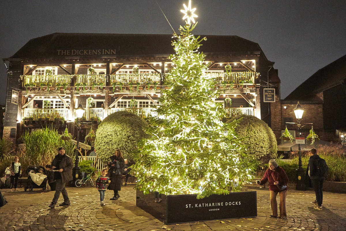 a christmas tree all lit up with lights in front of a fairy light decorated pub - the dickens inn