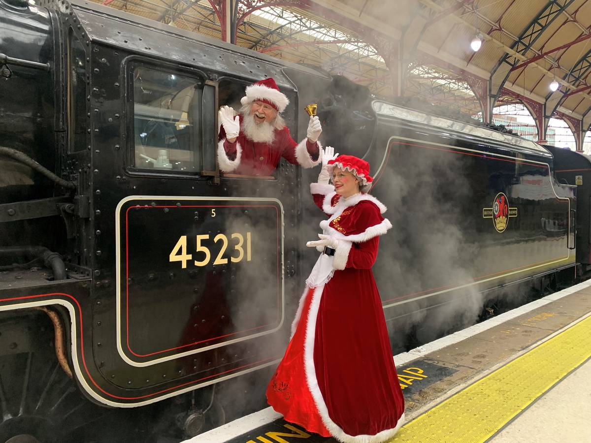 Santa and Mrs Claus outside a vintage steam train pulled into a station platform