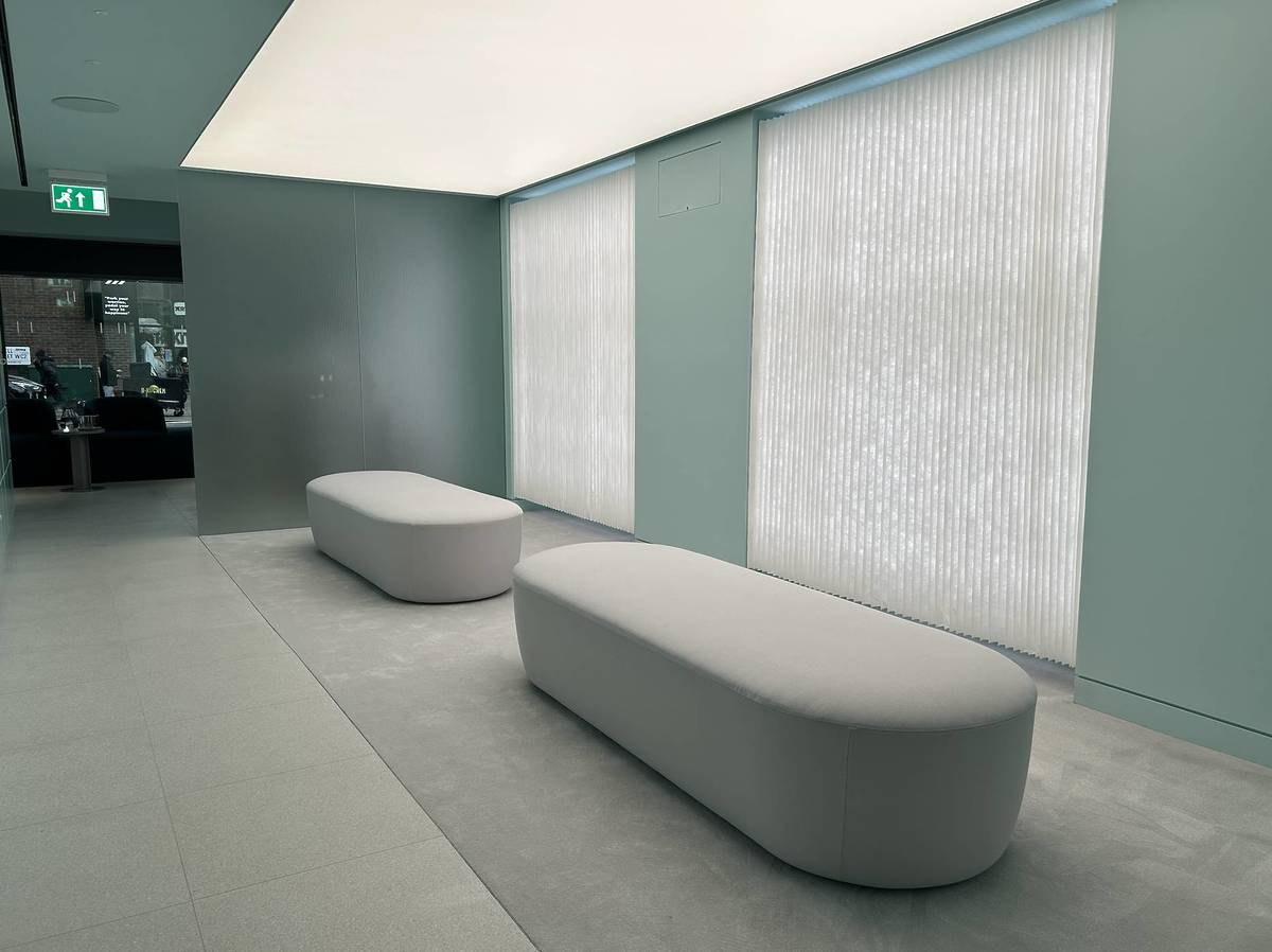 Two white benches sit in a brightly lit room with 2 white curtains behind them