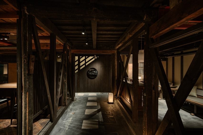 Photograph of a dark, warmly lit corridor made with timber beam structures separating two living areas of the house.