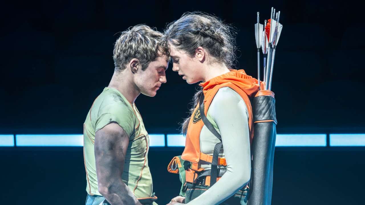 A man and woman facing each other. The Hunger Games on Stage - Euan Garrett (Peeta Mellark), Mia Carragher (Katniss Everdeen). Photo by Johan Persson