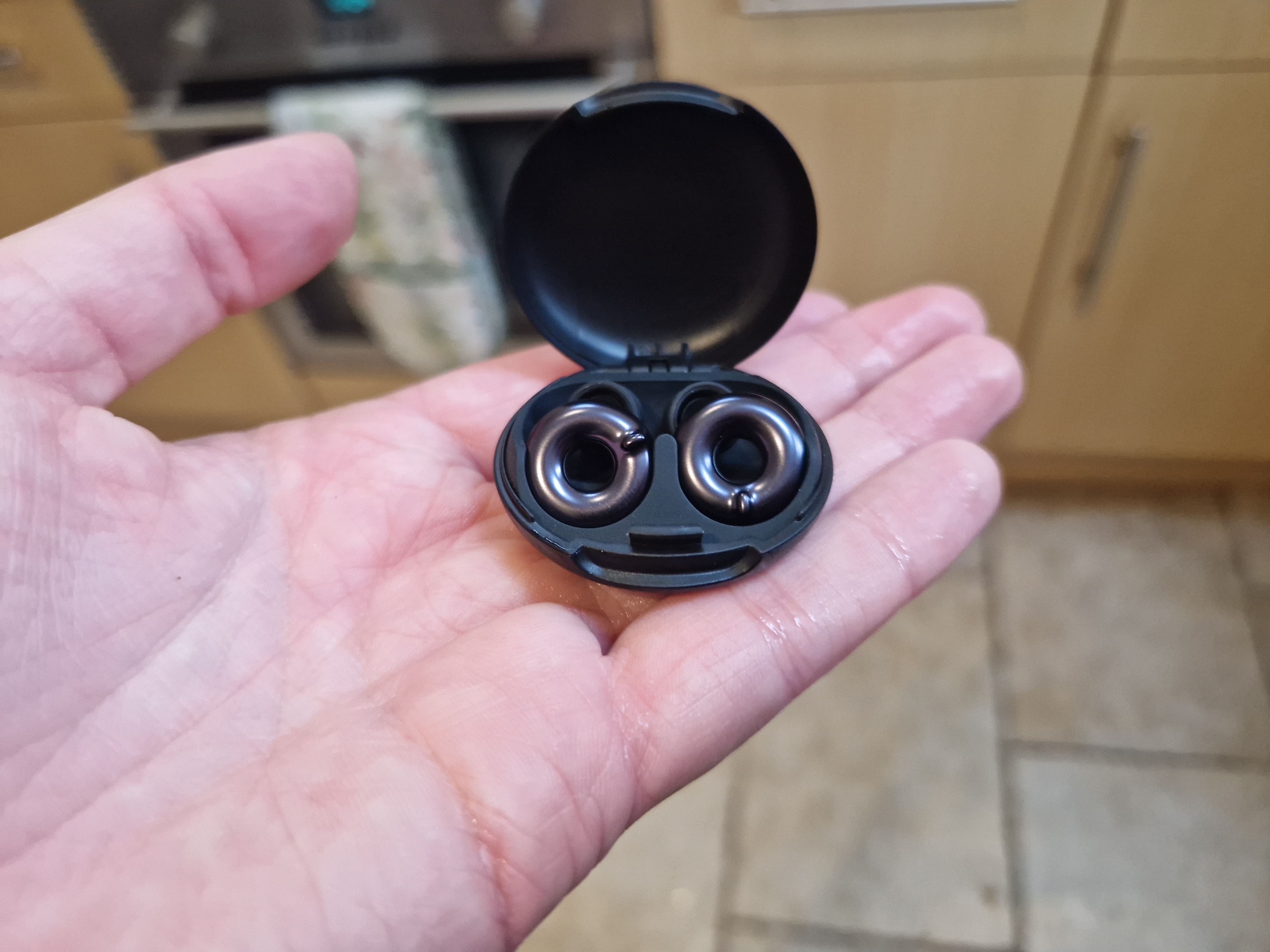 Black earbuds in an open case in someone&rsquo;s palm