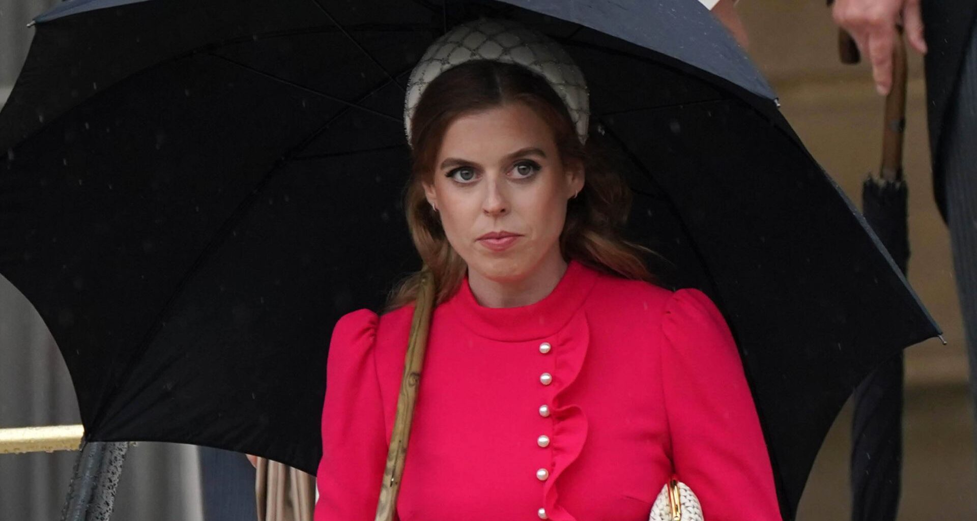 Princess Beatrice wears a red dress and carries a black umbrella while walking in front of sister Princess Eugenie at the Sovereign&#039;s Garden Party at Buckingham Palace on May 21, 2024