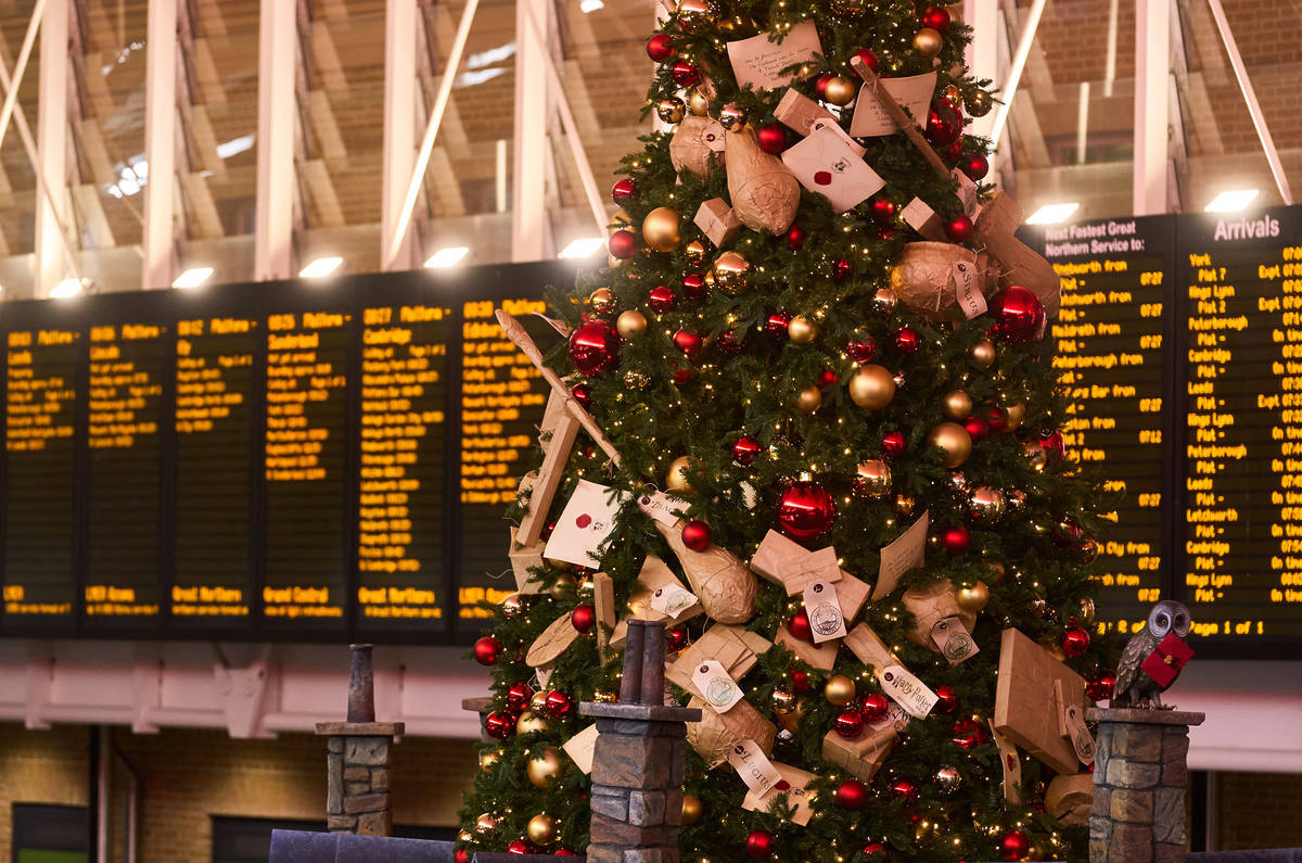 baubles and letters adorning a harry potter themed christmas tree, with the departure board for king's cross visible in the background