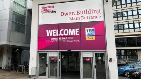 BBC Sheffield Hallam University is a modern building with bright pink and purple branding which says Owen Building Main Entrance