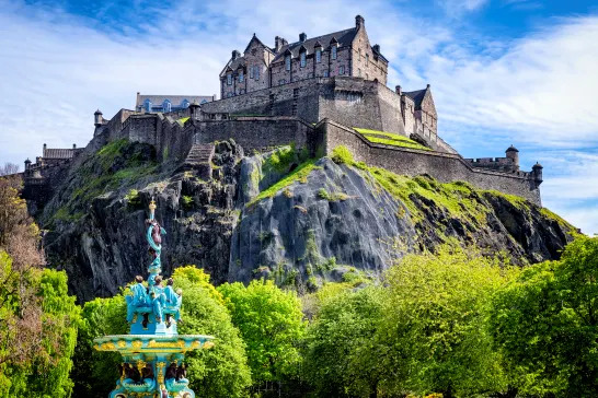 A view of Edinburgh Castle on a sunny day. The Ross Fountain is in the foreground and the netting over the rockface of the castle is visible in the background.