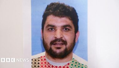 Young 18 year old man sits in the passenger seat of a black VW car, his arm resting on the open window as he looks to camera