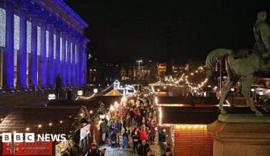 Liverpool Christmas Market at night showing traditional wooden chalets lit up on St George's Plateau with St George's Hall lit up with white lights.