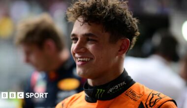 Lando Norris smiling after winning the Sao Paulo Grand Prix, with Max Verstappen visible in the background