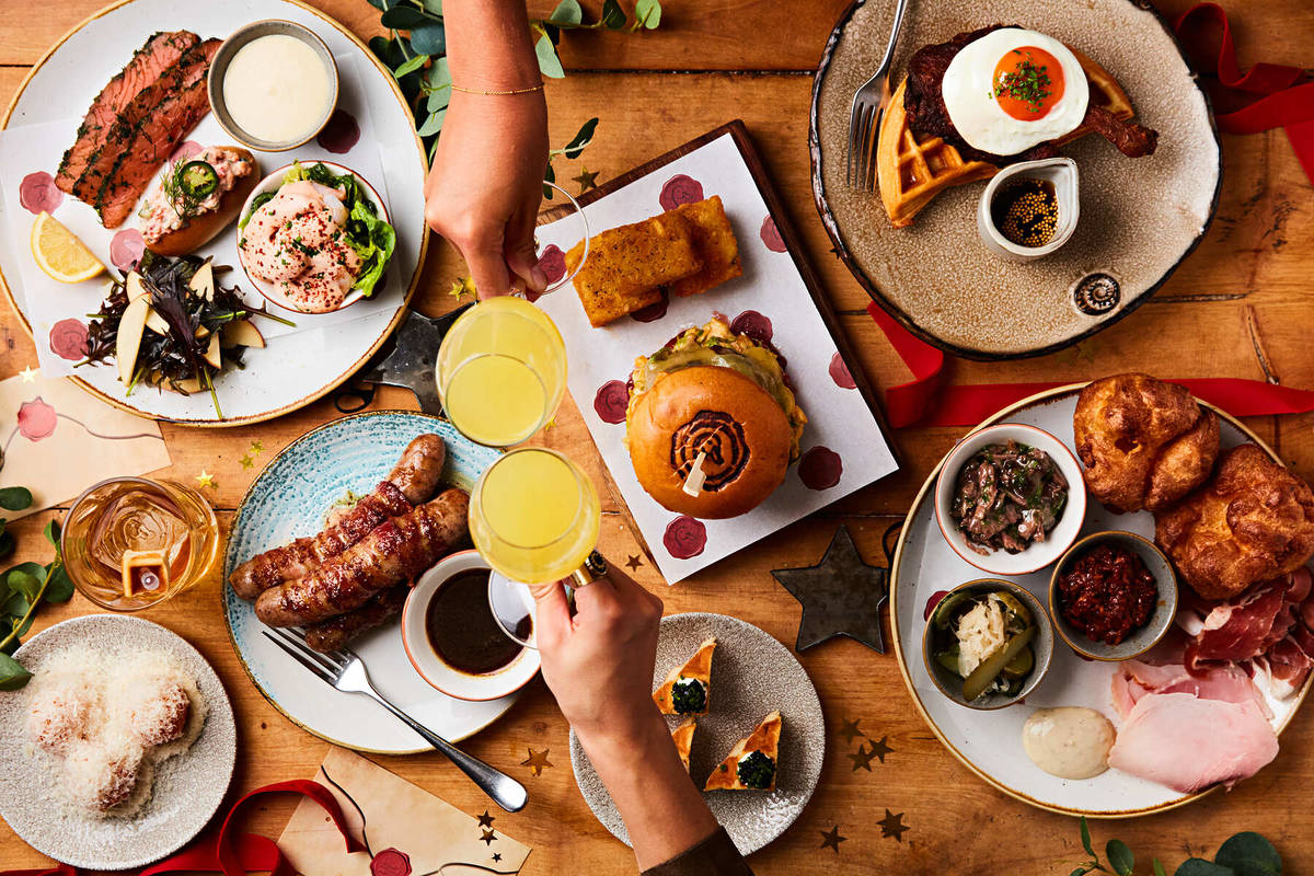 an array of festive brunch dishes on a table, as seen from above, with two glasses of mimosa cheersing together over the food