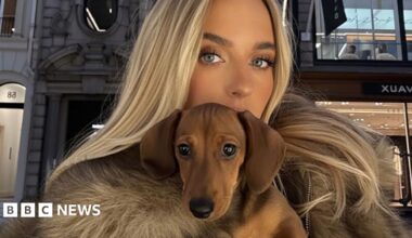 A woman with blond hair holding a Dachshund dog - the dog is AI generated.