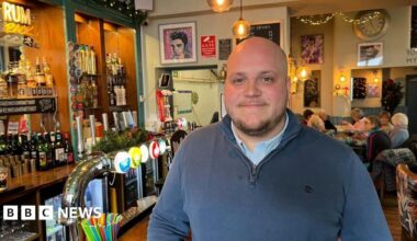 A picture of Rob Moore in his pub. He is wearing a navy blue shirt and is smiling and looking at the camera.