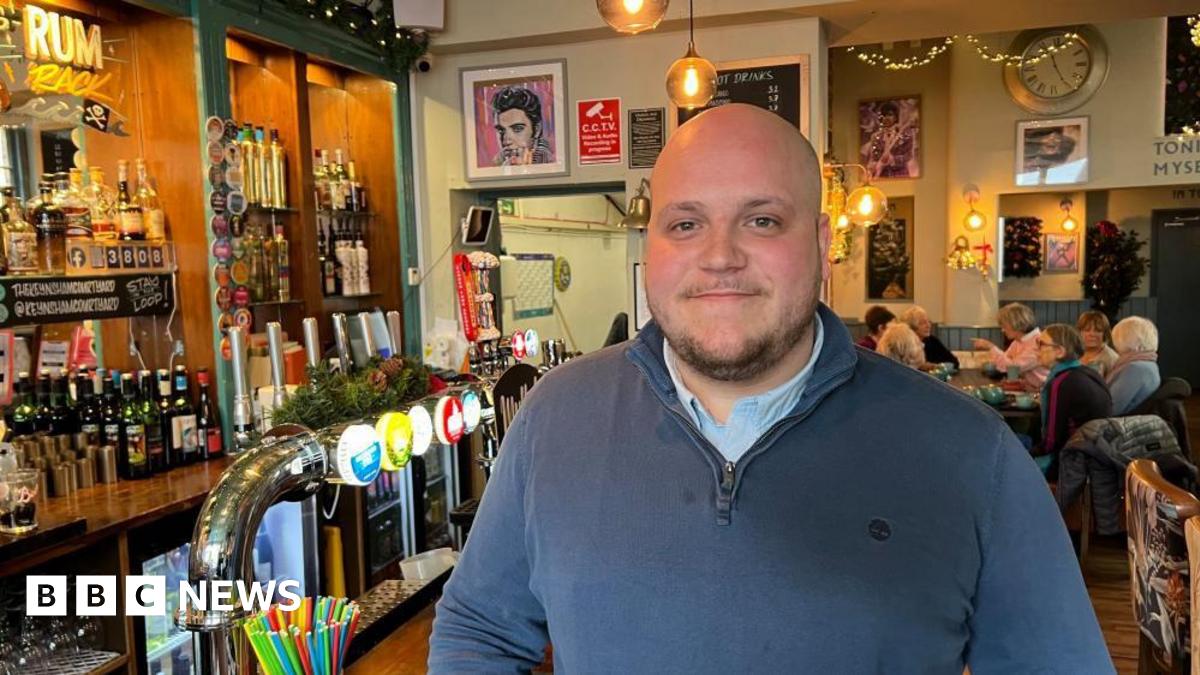 A picture of Rob Moore in his pub. He is wearing a navy blue shirt and is smiling and looking at the camera.
