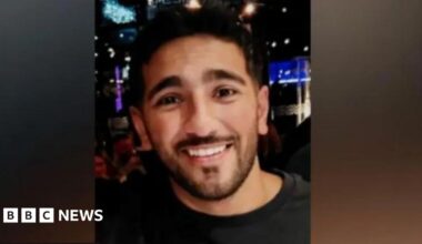 Image of Rehaan smiling at the camera. He is wearing a black t-shirt. Behind him a nightclub can be seen.